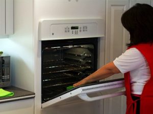 A woman is holding an oven door open.