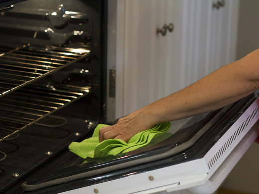 A person cleaning an oven with a green cloth.