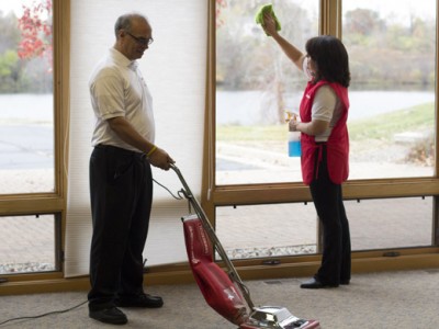 A man and woman are using a vacuum to clean the floor.