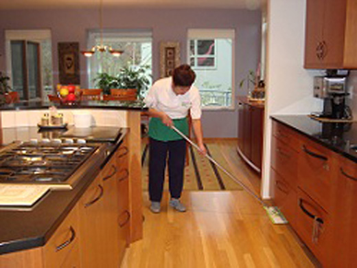 A woman in the kitchen cleaning the floor.